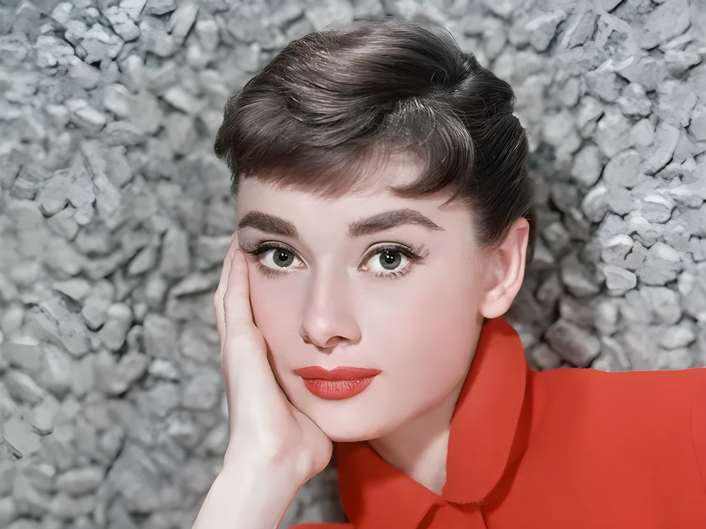 Audrey Hepburn posing with her hand on her face wearing a red outfit