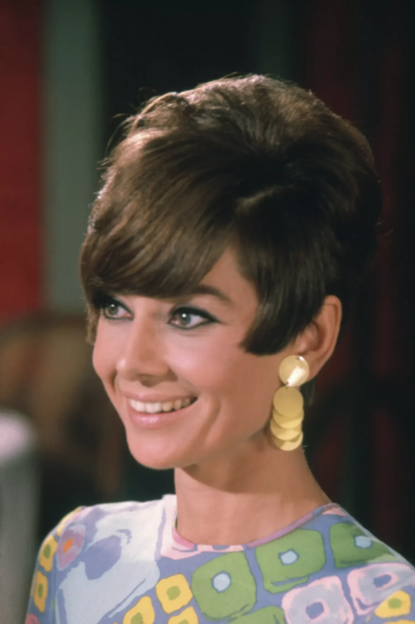 Audrey Hepburn wearing gold, circular earrings, a colorful top, and a beehive pixie hairstyle