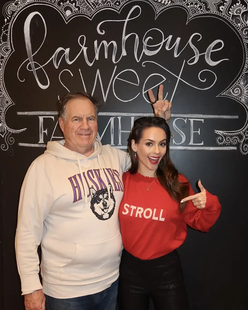 Bill Belichick and Jordon Hudson pose in front of a chalkboard sign.