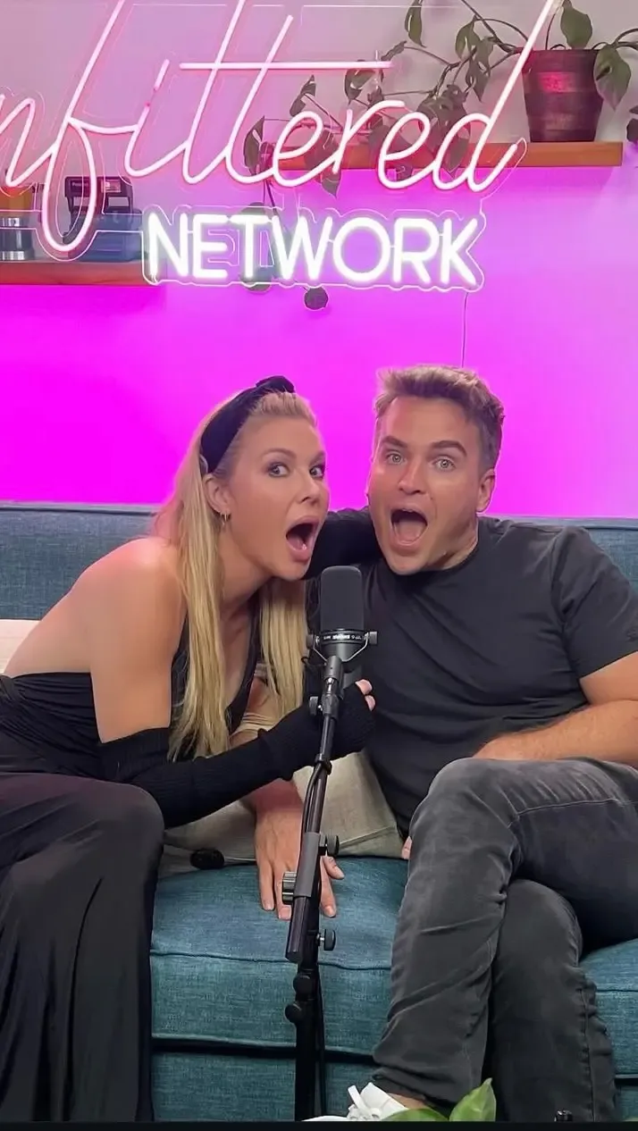 Brandi Glanville and podcast co-host James Maas sit on a couch in front of an Unfiltered Network sign, both with their mouths open in surprise.