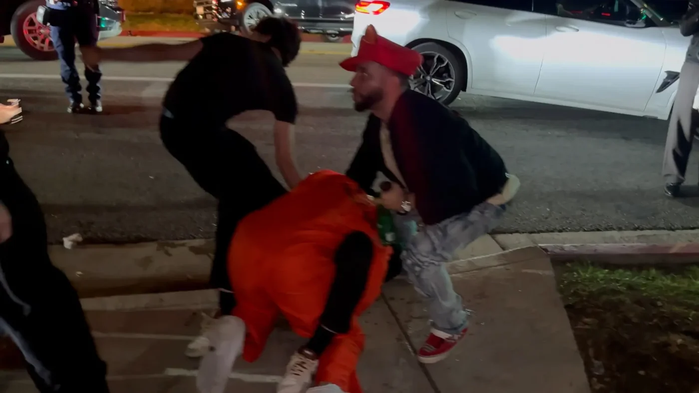 Bryce Hall, dressed in an orange prison jumpsuit, is on the ground during a physical altercation with several men outside a Halloween party.
