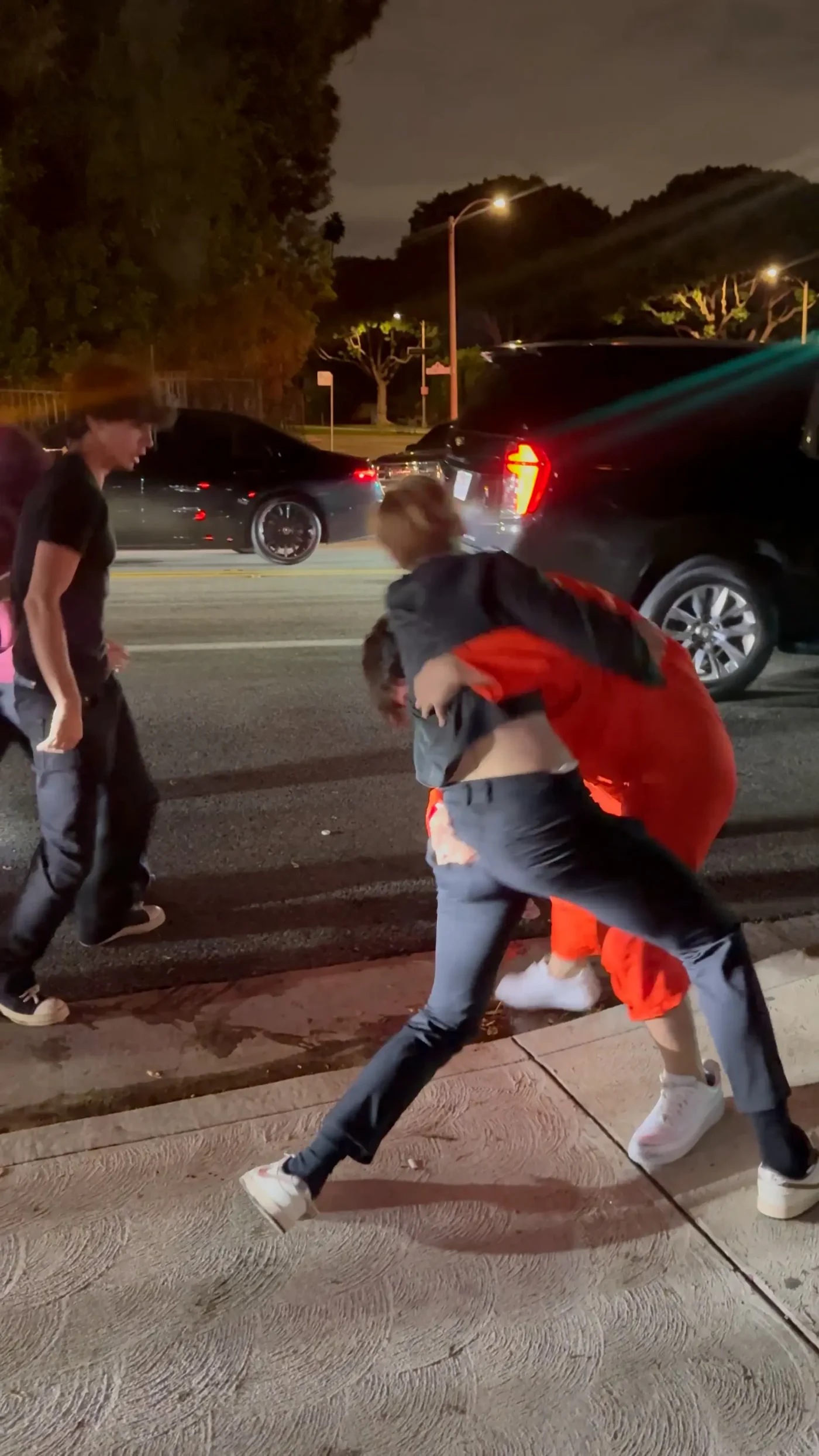 Bryce Hall in an orange prison jumpsuit is wrestled to the ground by a man on a sidewalk at night.