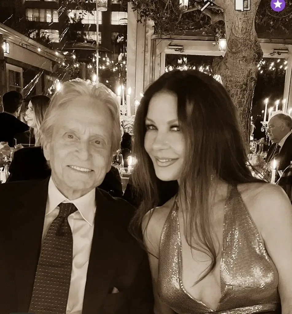 Catherine Zeta-Jones and Michael Douglas sitting at a table in evening wear smiling for a selfie