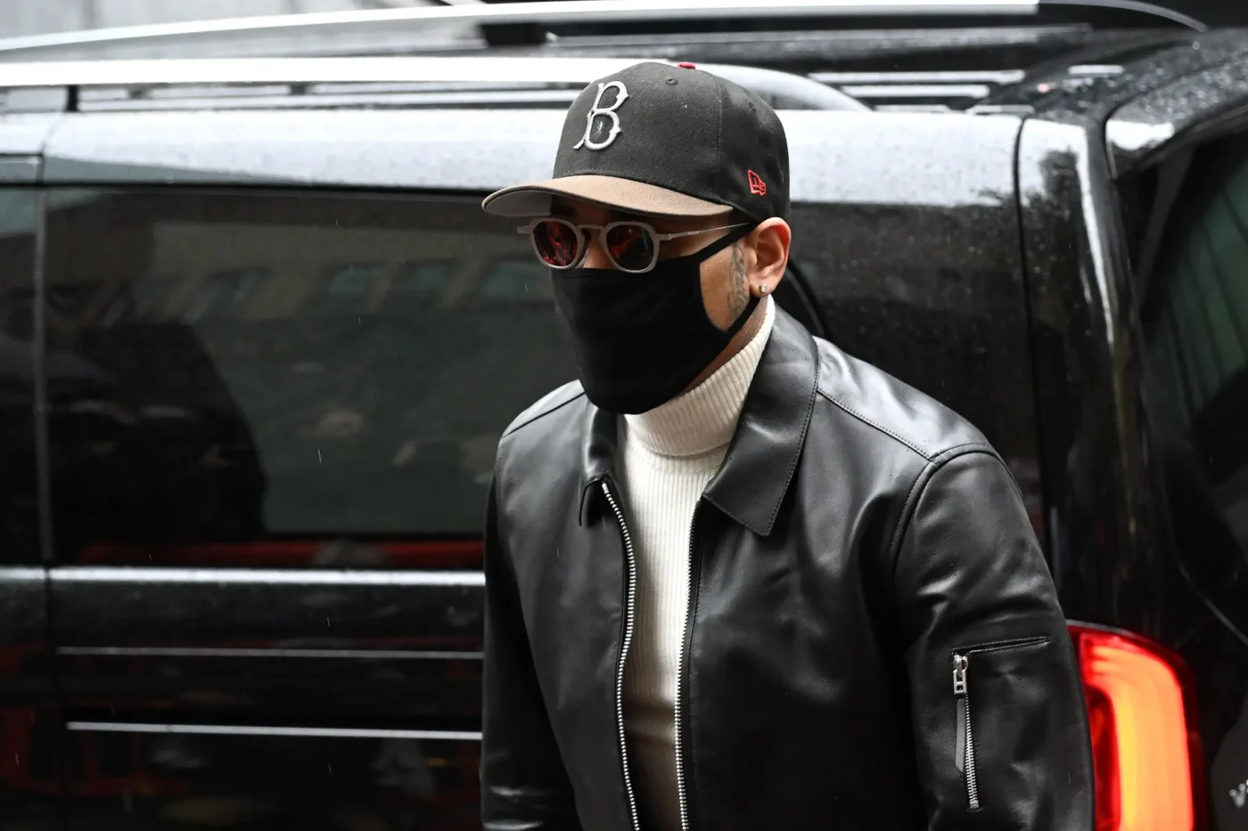 Chris Brown arriving at court in London wearing a black leather jacket, cap, sunglasses, and face mask.