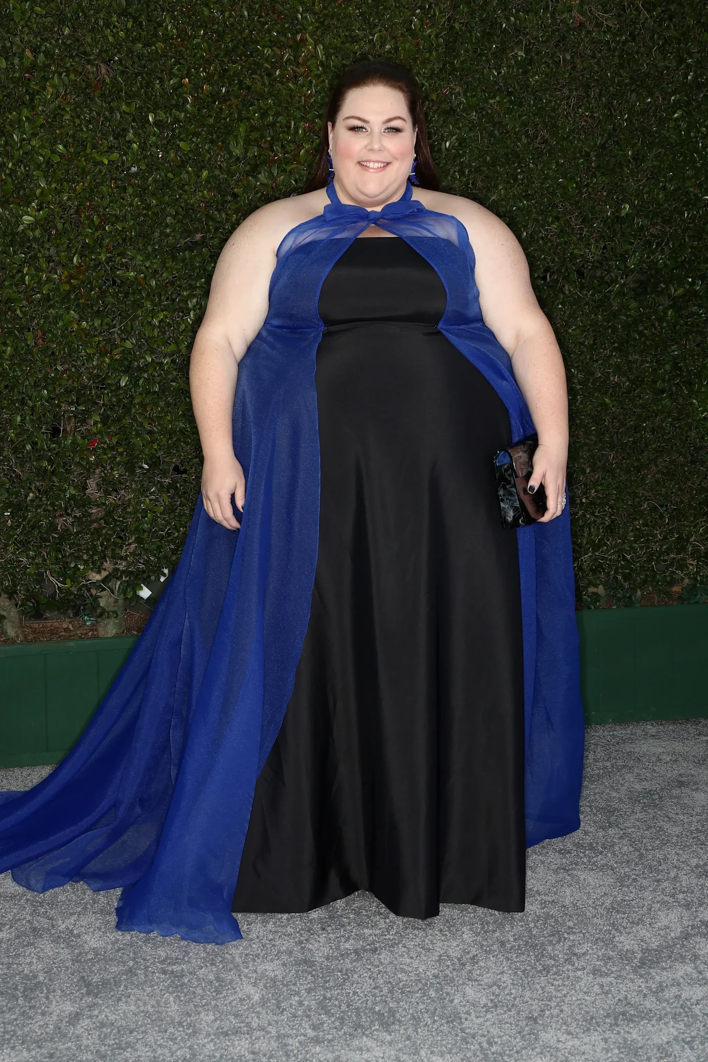 Chrissy Metz poses on the red carpet in a black gown with a sheer blue overlay.