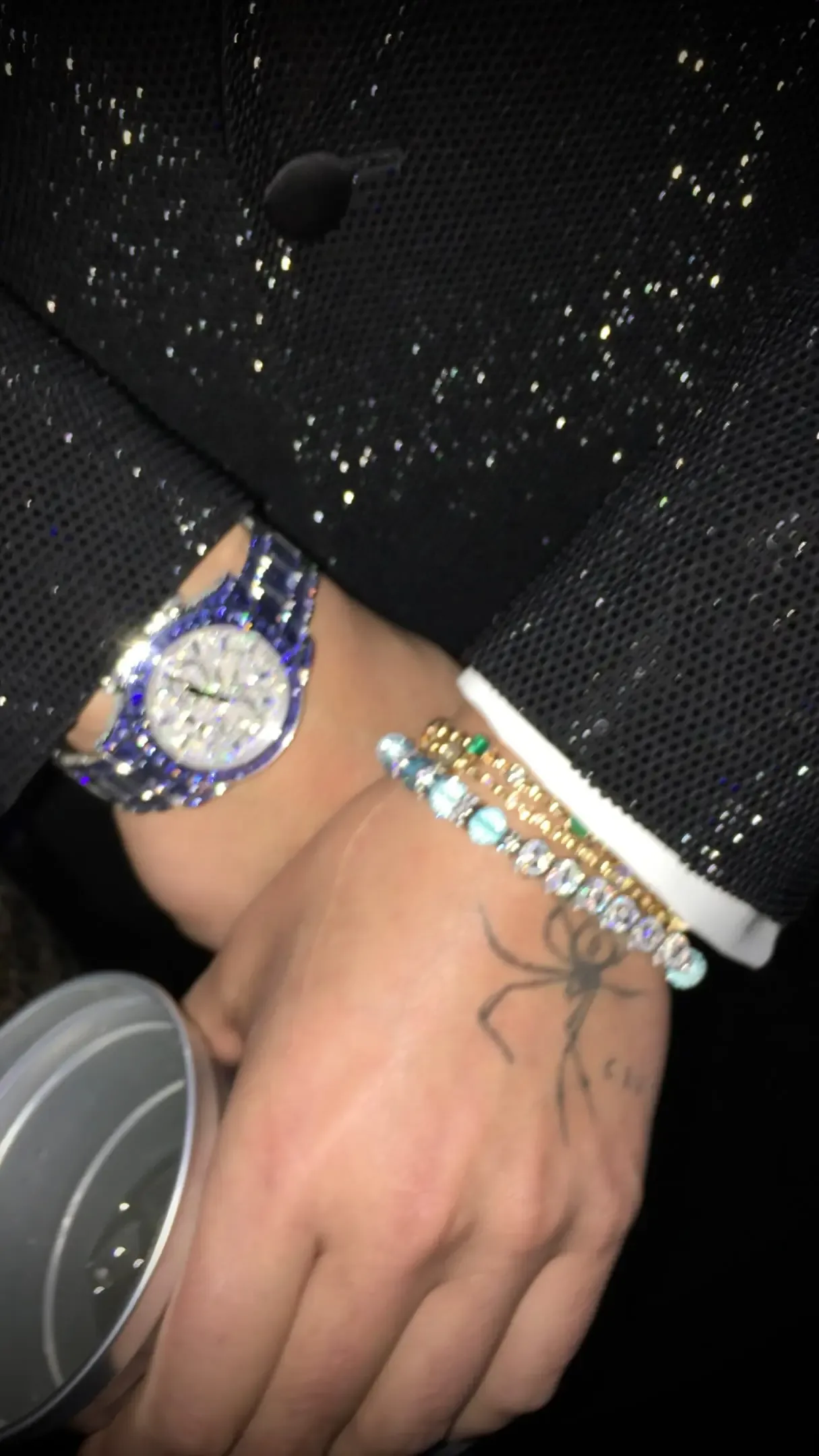 Close-up of a person wearing a sparkling diamond watch and bracelets on their wrists.