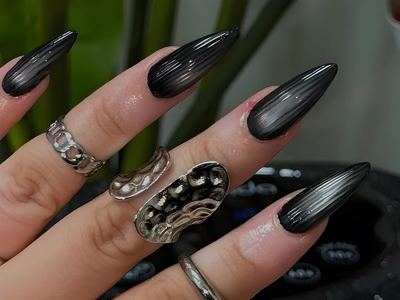 Closeup of a hand with long sharp black gradient nails and multiple silver rings
