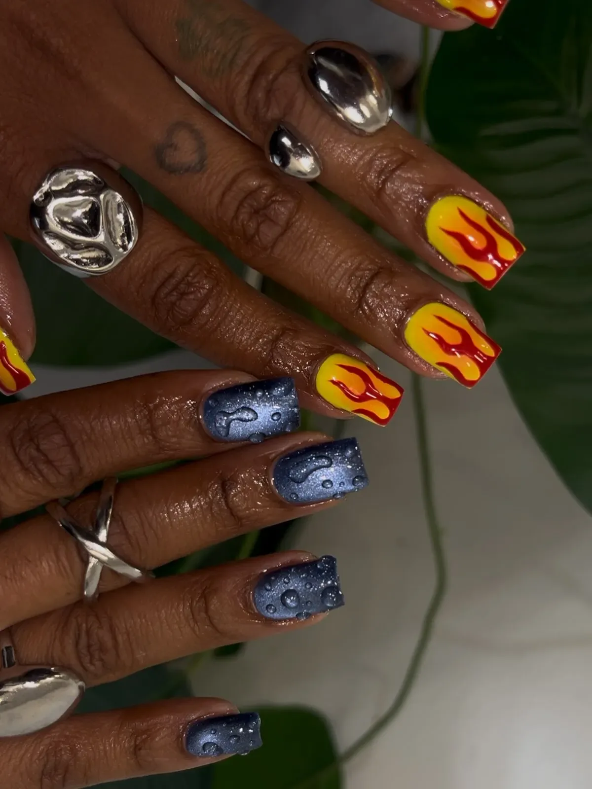 Closeup of hands showcasing manicure with flame designs and metallic accents on nails