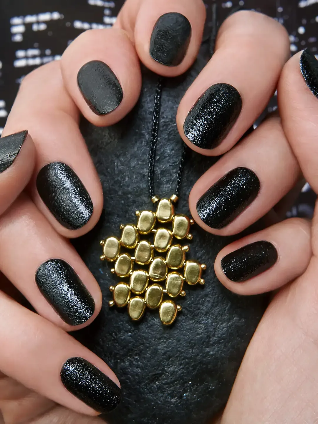 Closeup of hands with manicured nails holding a textured object with a pendant