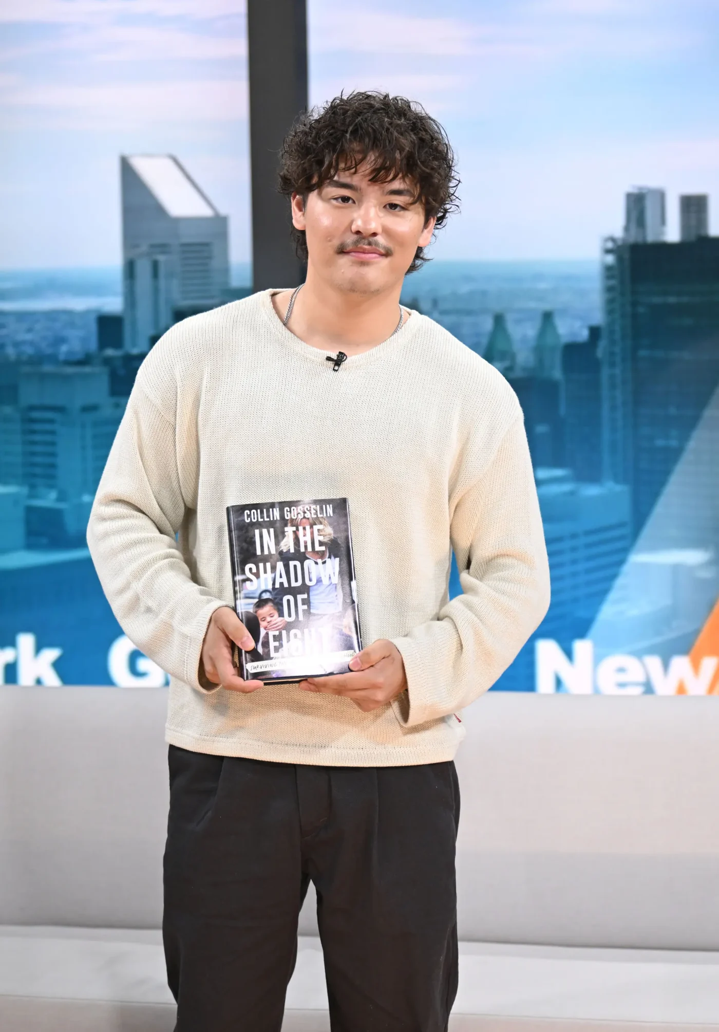 Collin Gosselin stands holding a copy of his book,