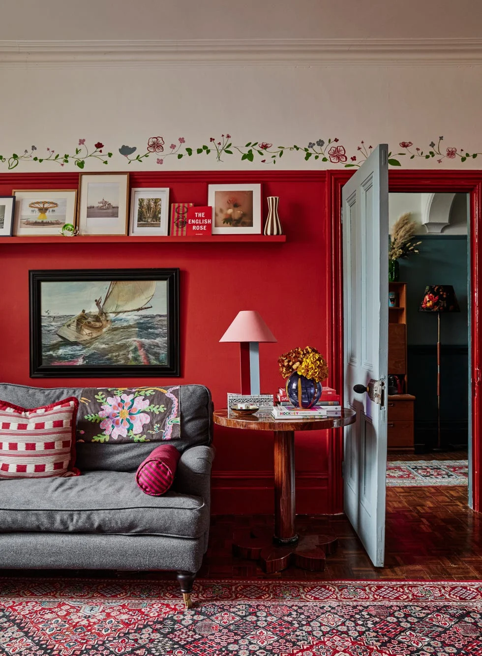cozy living room with grey couch, red walls, floral decorations, and a partially open blue door.