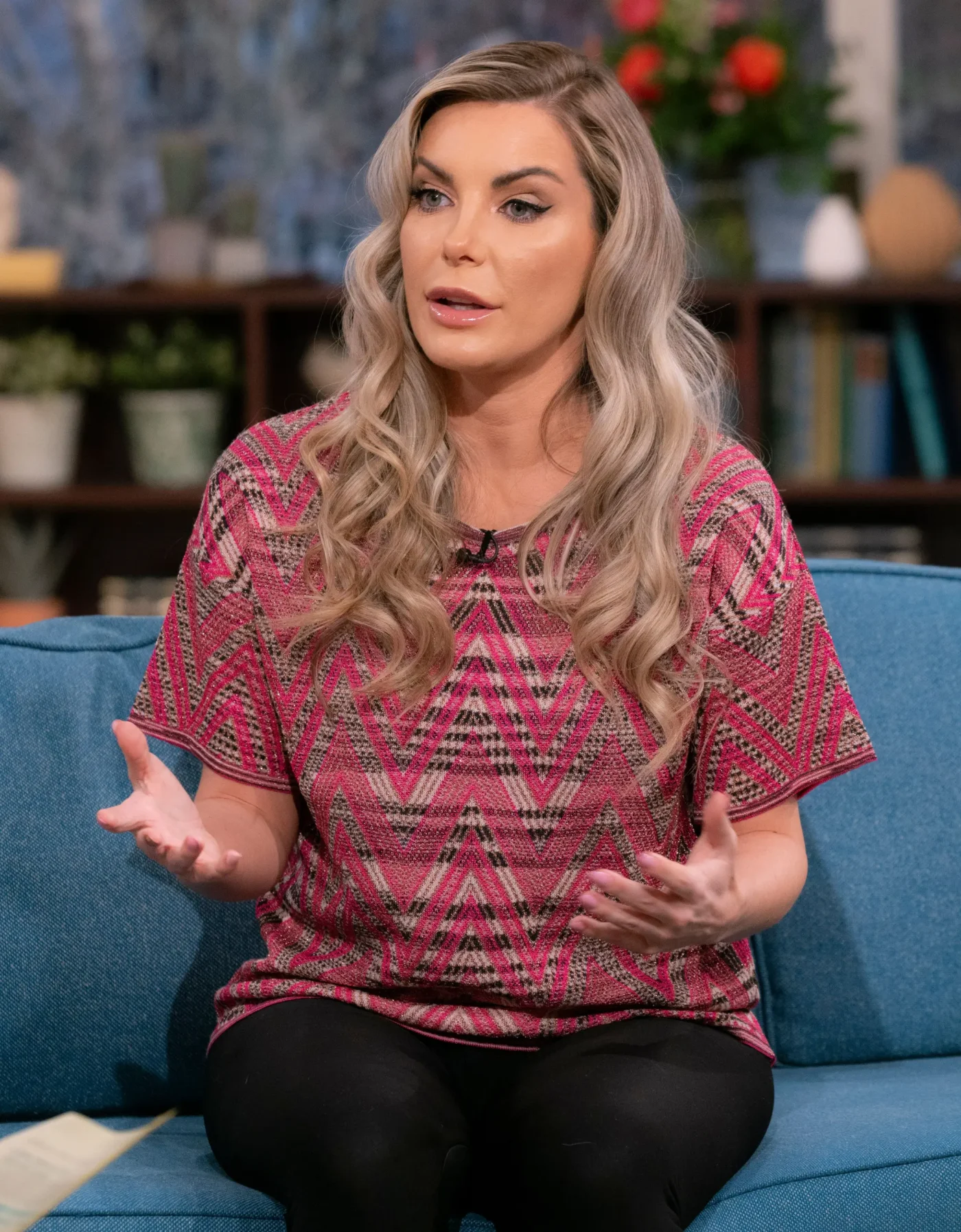 Crystal Hefner seated on a blue sofa during an interview.