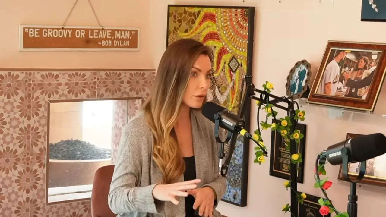 Crystal Hefner sitting in front of a microphone in a room with a decorated wall and framed photos.