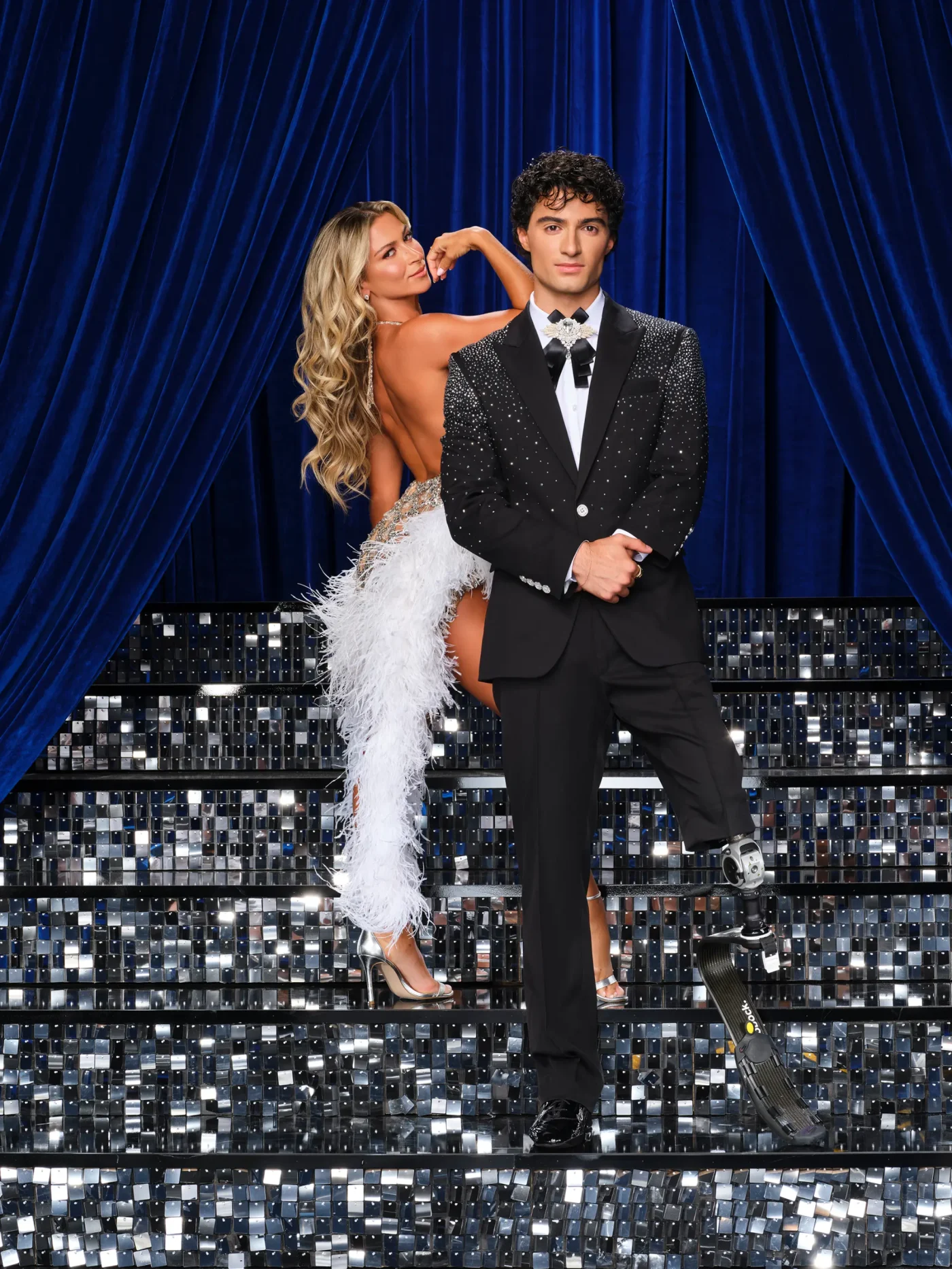 Daniella Karagach and Ezra Frech pose in front of blue curtains on a sparkling staircase.