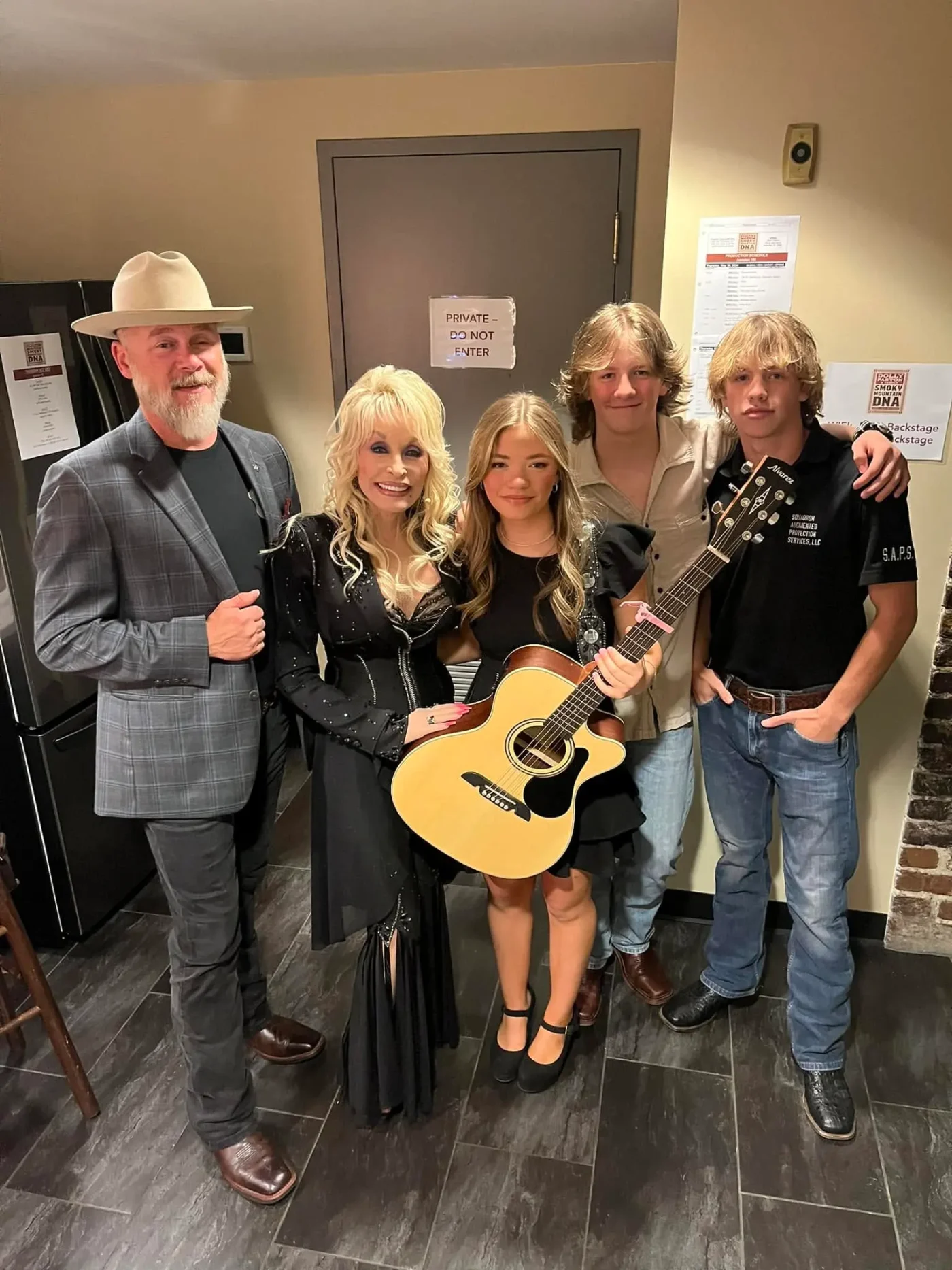 Dolly Parton and four other people posing for a photo indoors, with one person holding an acoustic guitar.