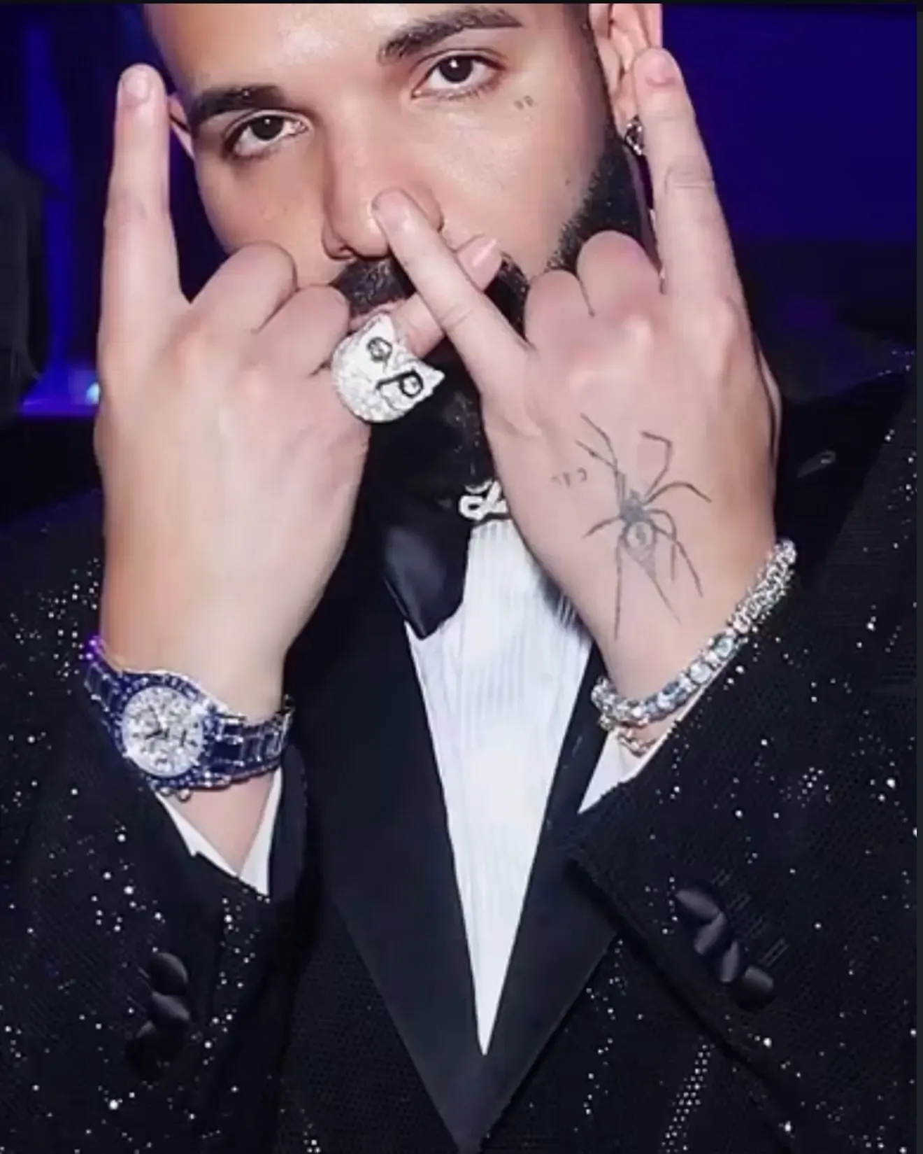 Drake wearing a diamond bracelet and rings while showing hand signs.