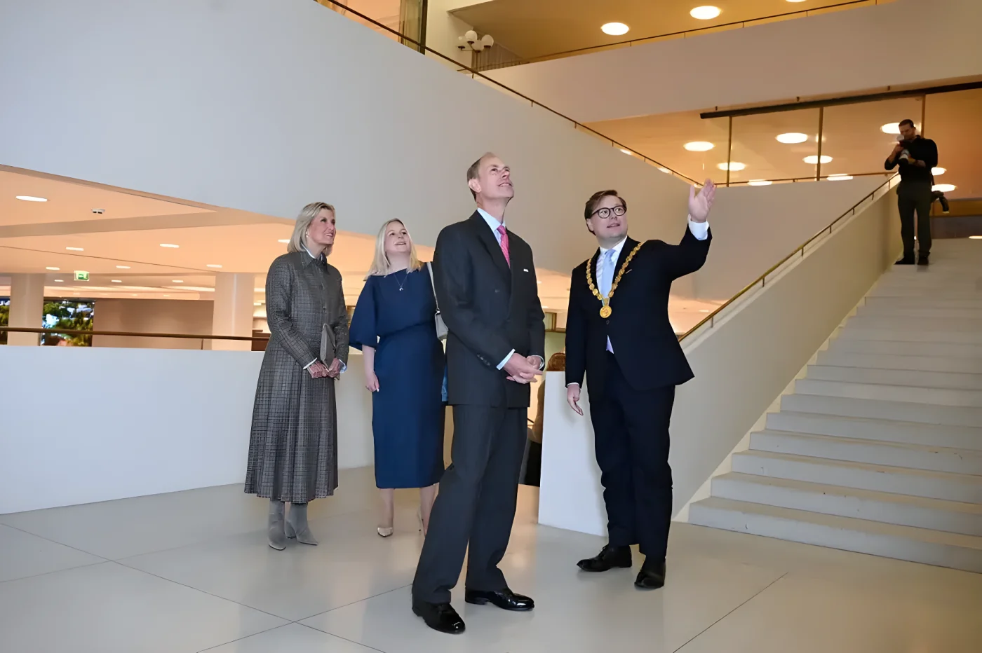 Duchess of Ediburgh stands with two other individuals in formal attire in a modern building.