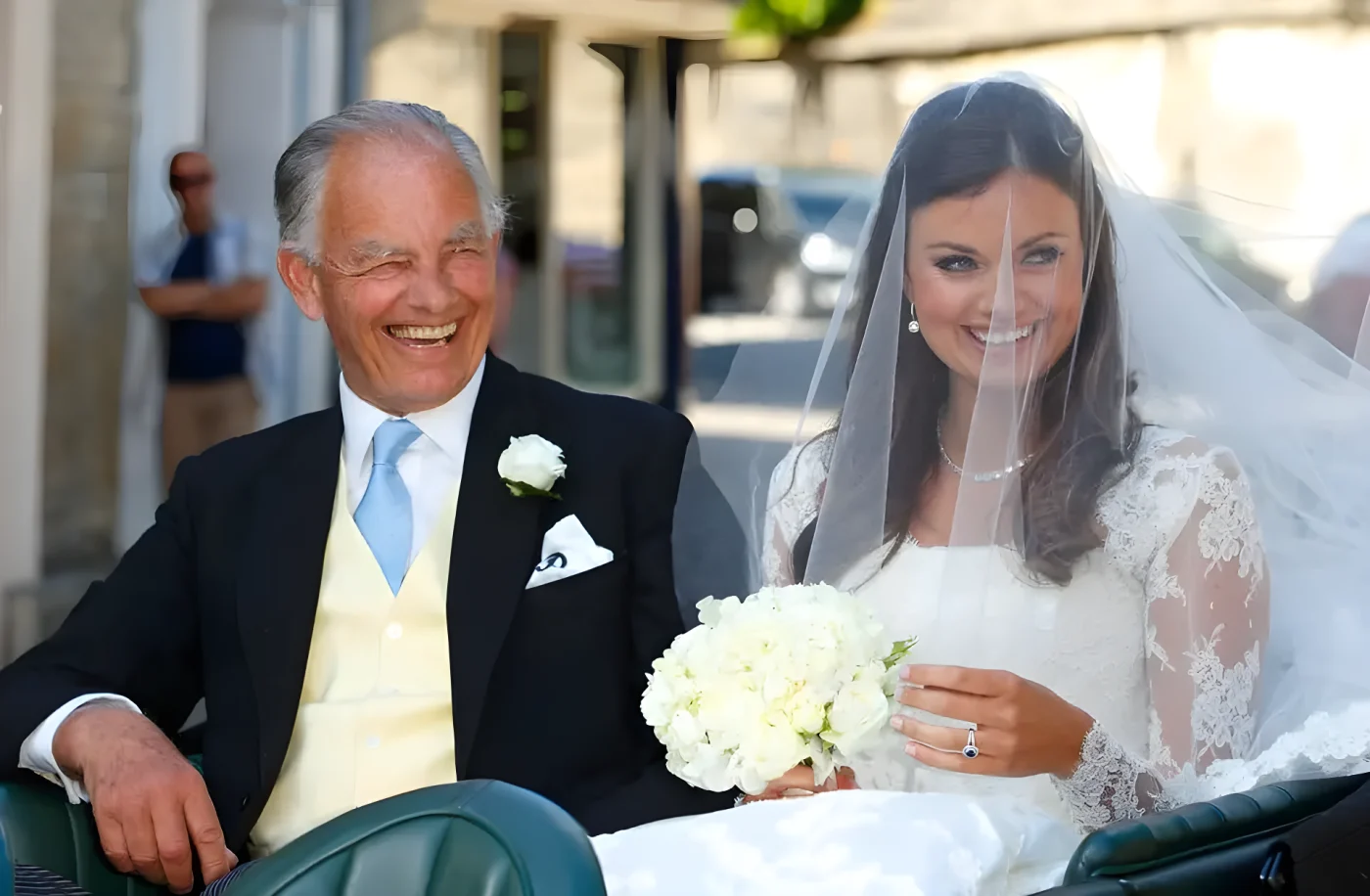 Elderly man and young woman, both smiling, seated in a vehicle. Woman holds a bouquet of white flowers.