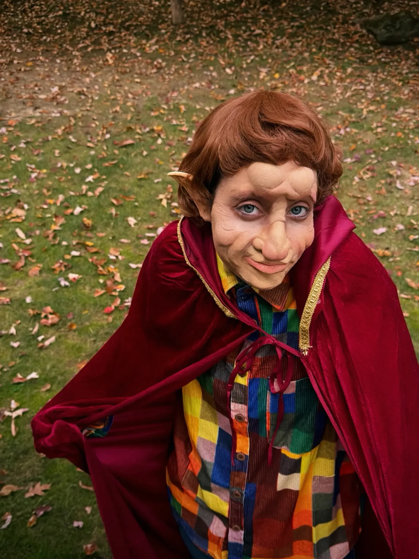 Elizabeth Gillies wearing a goblin Halloween costume in a yard covered in fallen leaves.