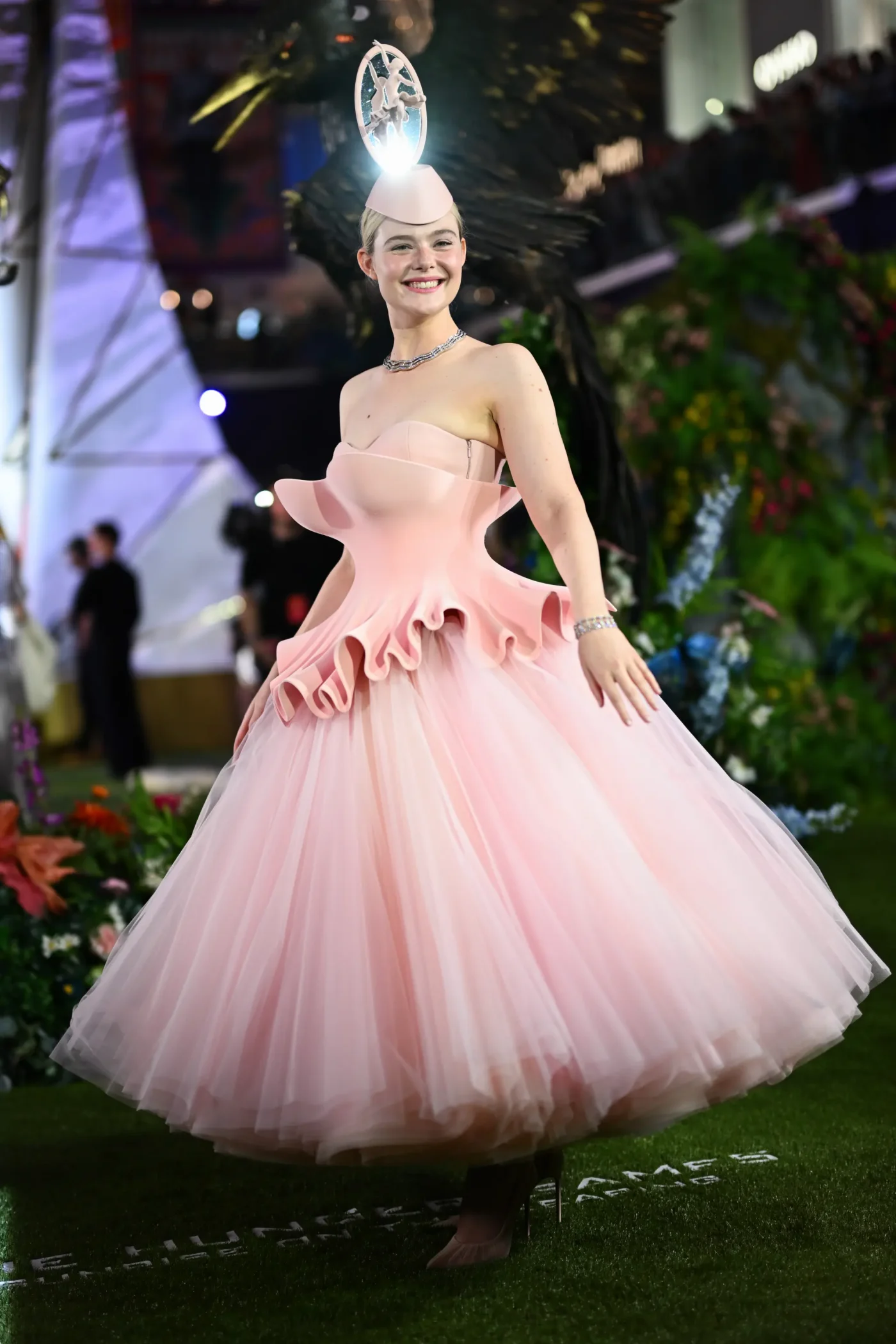 Elle Fanning wearing a pale pink structured gown and matching headpiece at a fan screening.