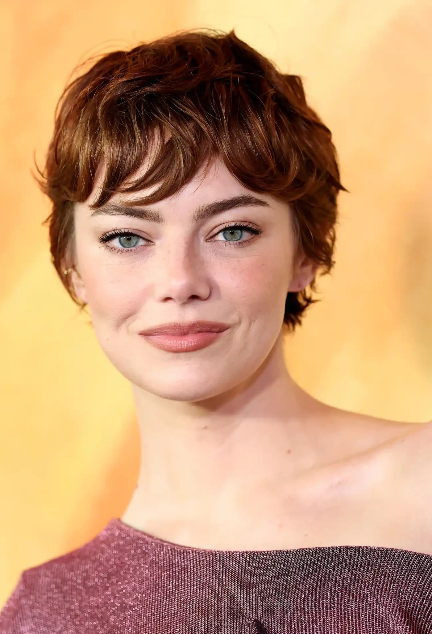 Emma Stone smiling in front of a neutral background