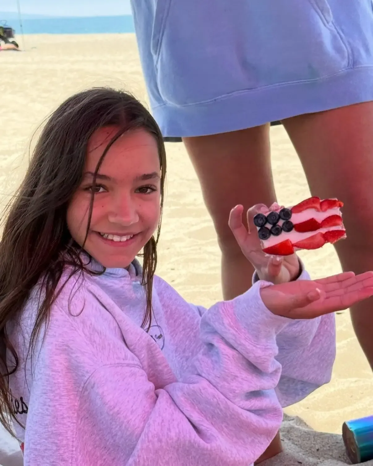 Fiona Lowe smiling on a beach while holding a slice of cake decorated to look like the American flag.