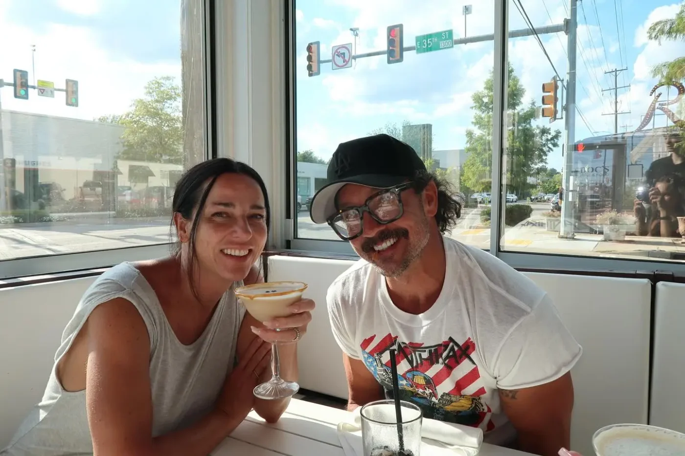 Former Hillsong pastor Carl Lentz and his wife Laura sit together at a restaurant table, smiling for the camera.