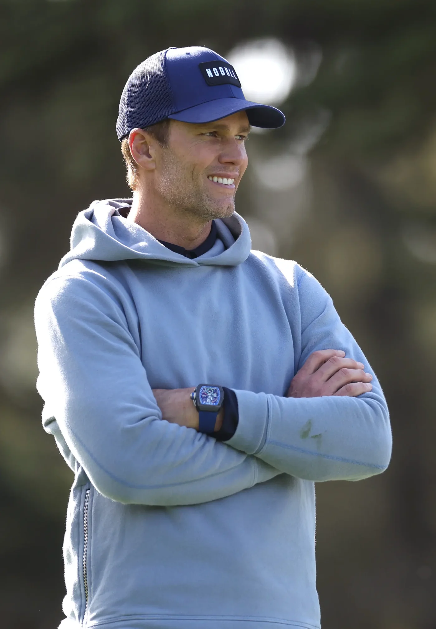 Former NFL quarterback Tom Brady wearing a blue hoodie and cap while looking on during the AT&T Pebble Beach Pro-Am.