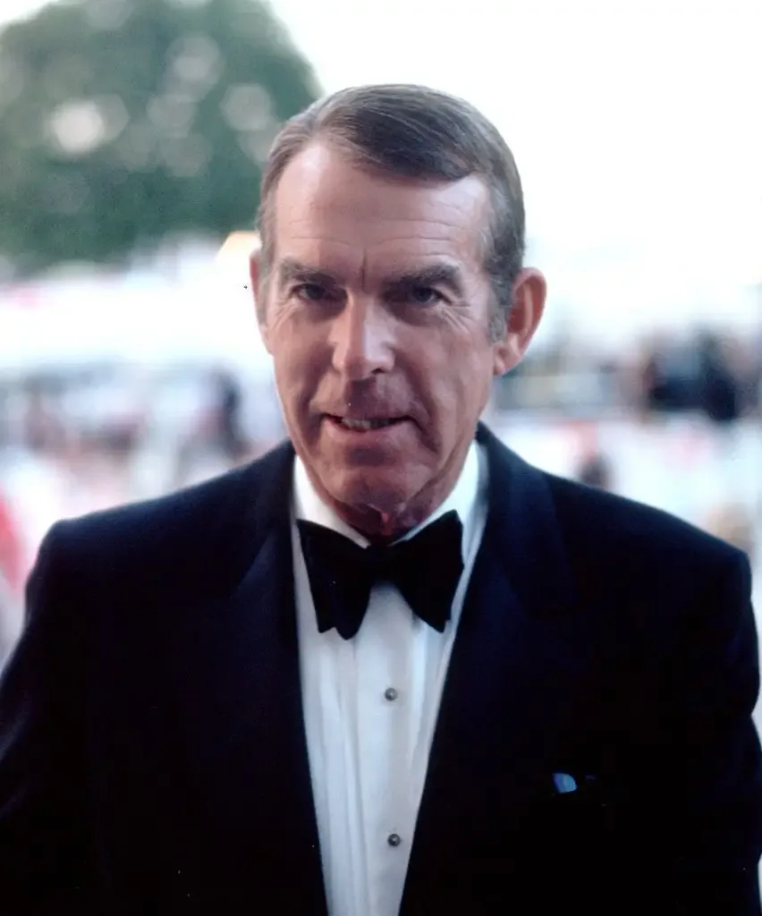 Fred MacMurray, in a black tuxedo with bow tie, looks directly at the camera outdoors.