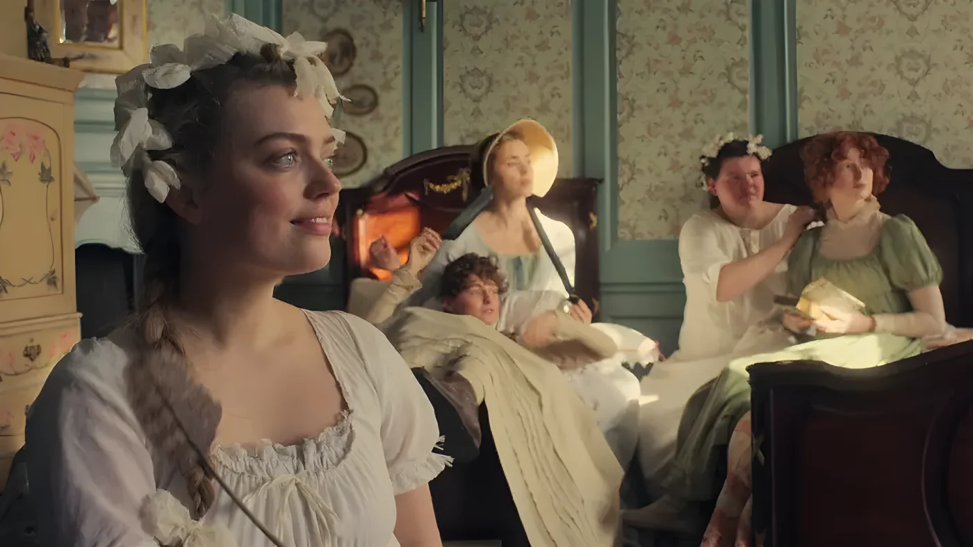 Freya Mavor in a white dress with a flower crown stands in a room with other women in period clothing.