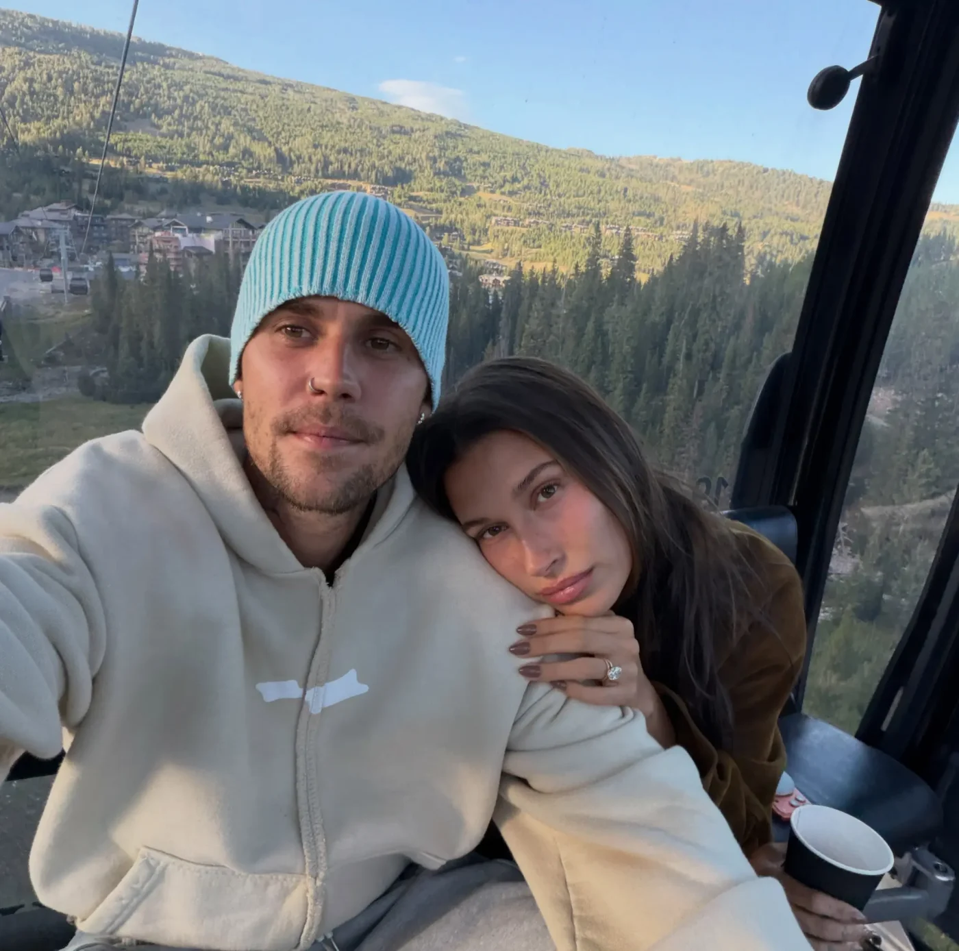Hailey and Justin Bieber pose together inside a gondola with a mountain landscape in the background.