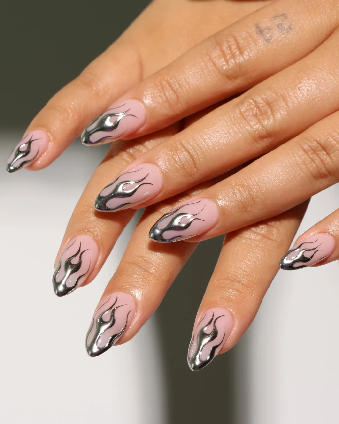 Hands with long pointed nails featuring a flame design with metallic accents