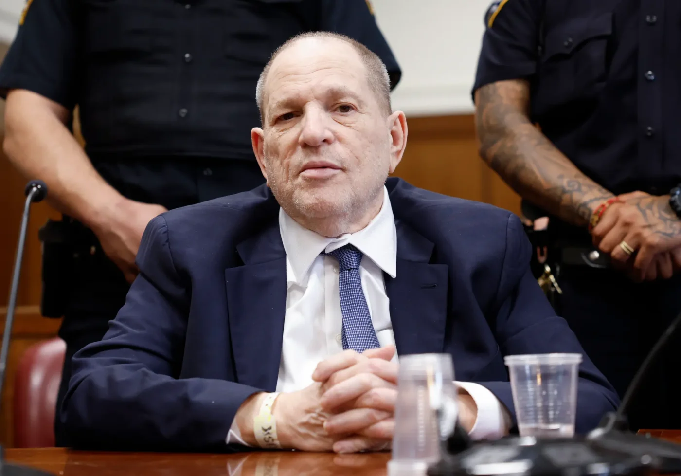 Harvey Weinstein sits in a courtroom flanked by police officers during his retrial.