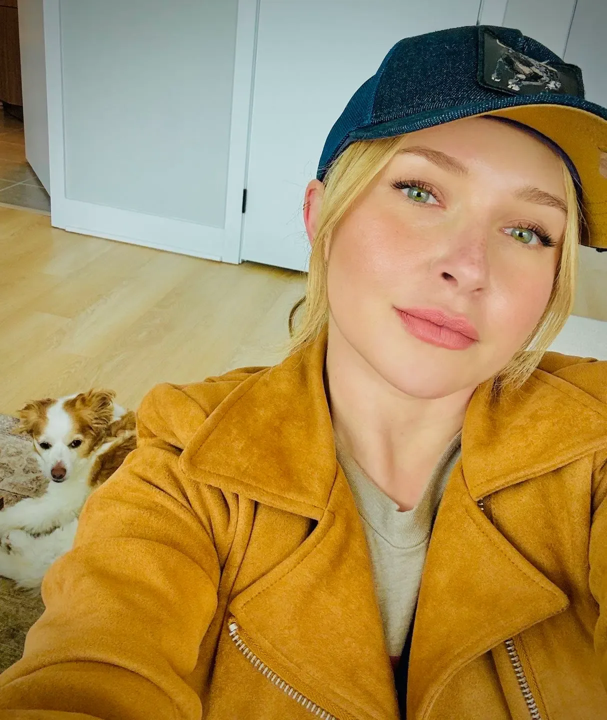 Hayden Panettiere wearing a cap and jacket, with a small dog sitting behind her on the floor.