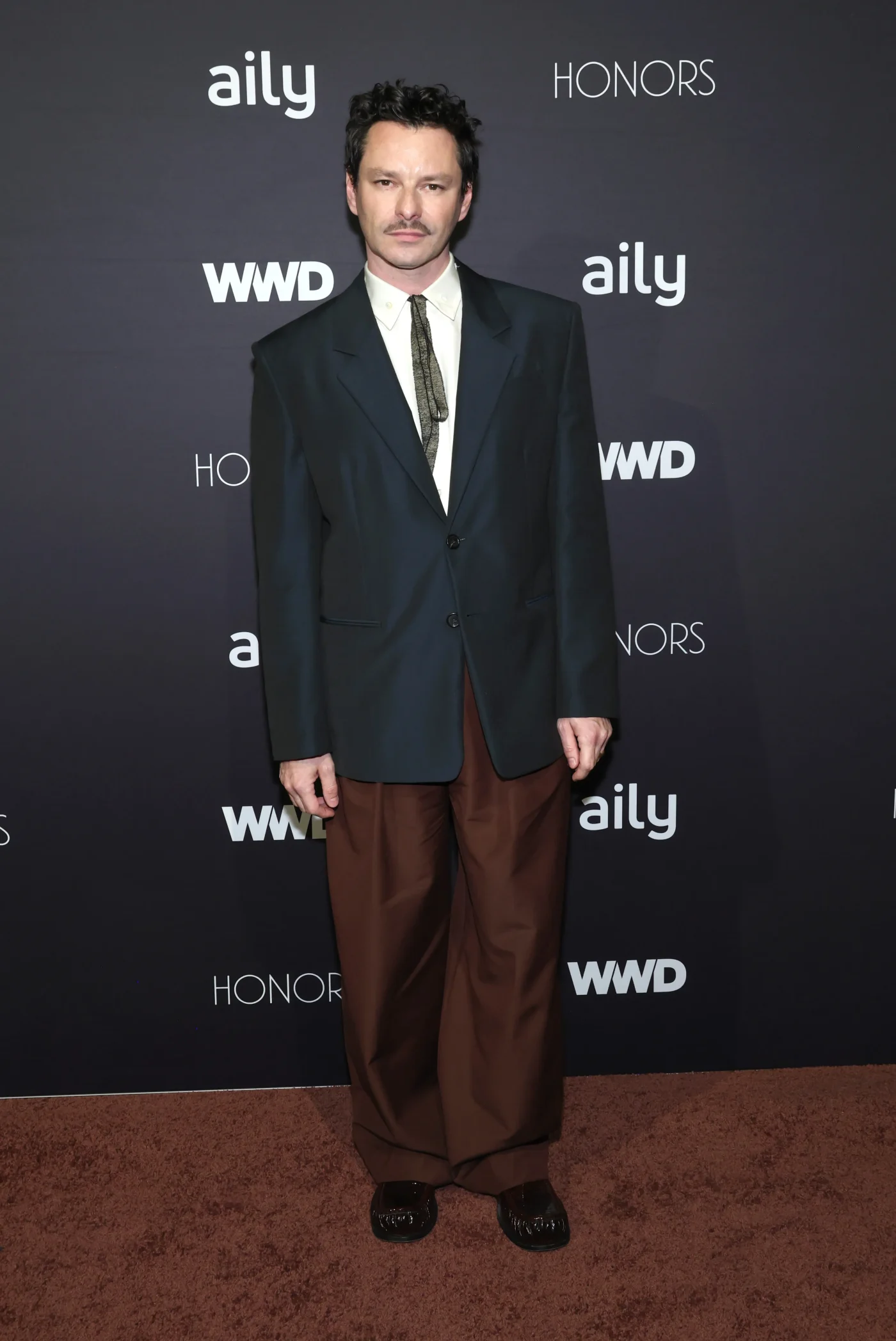 Henry Zankov wearing a dark blazer, white shirt, and brown trousers at the WWD Honors.