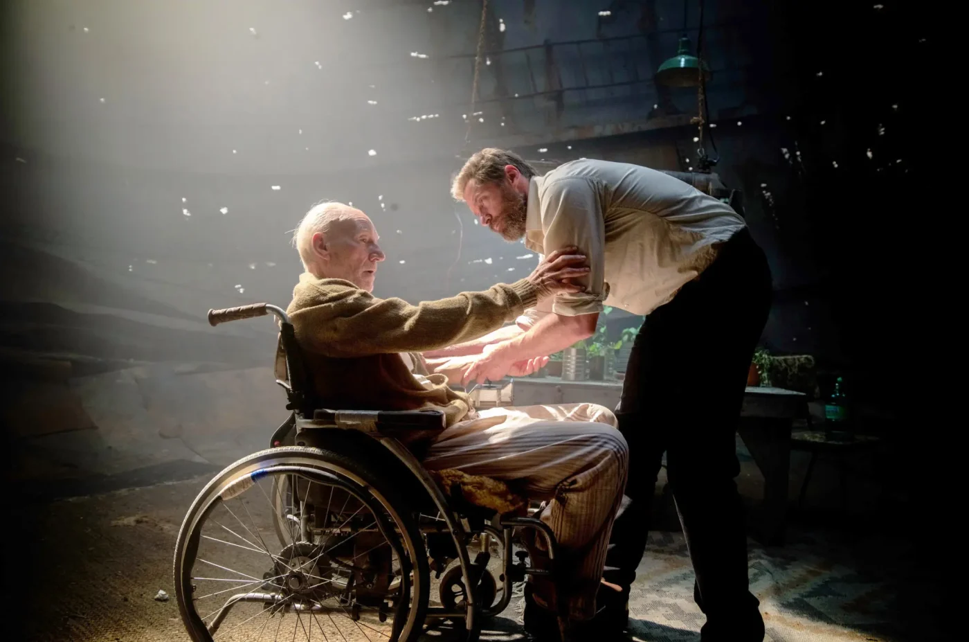 Hugh Jackman as Logan stands beside Patrick Stewart as Charles Xavier sitting in a wheelchair.