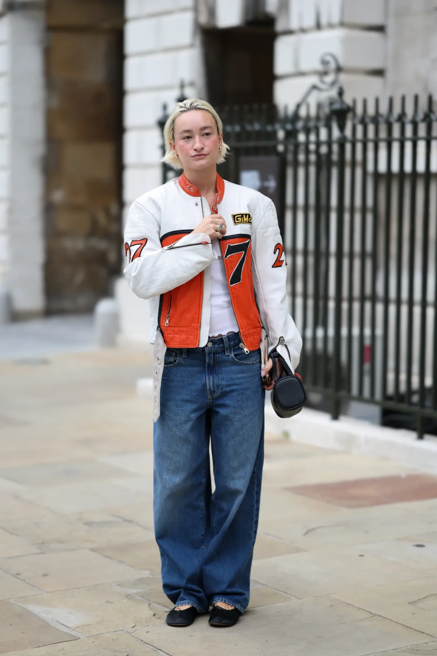 Individual in a street setting with a white jacket and blue jeans holding a small bag