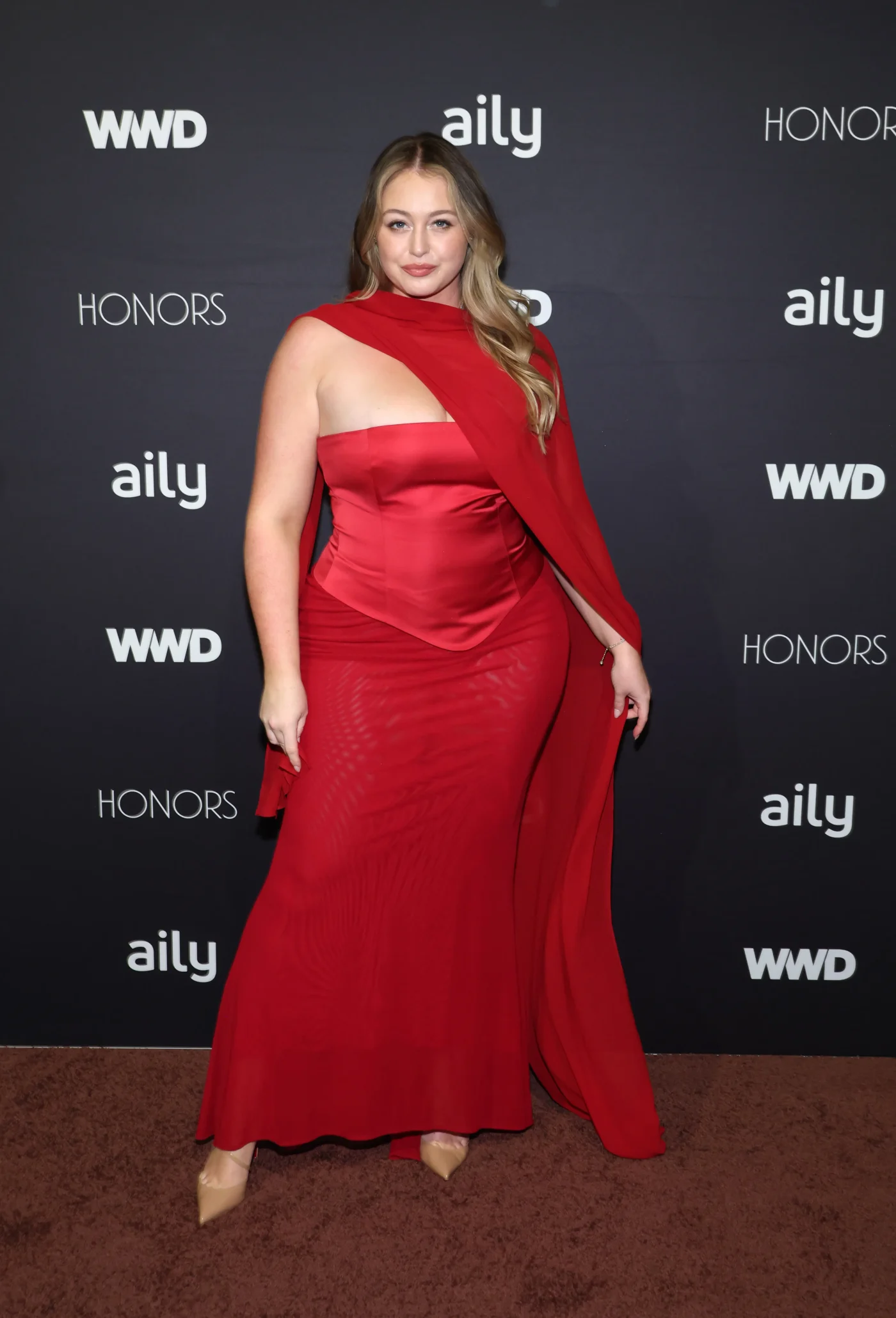 Iskra Lawrence poses in a red gown on the red carpet at the WWD Honors.