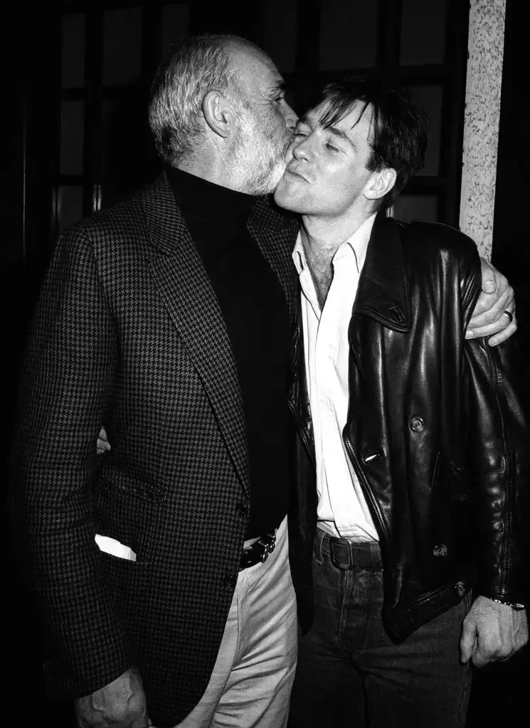 Jason Connery kisses an older man on the cheek. Both wear jackets.