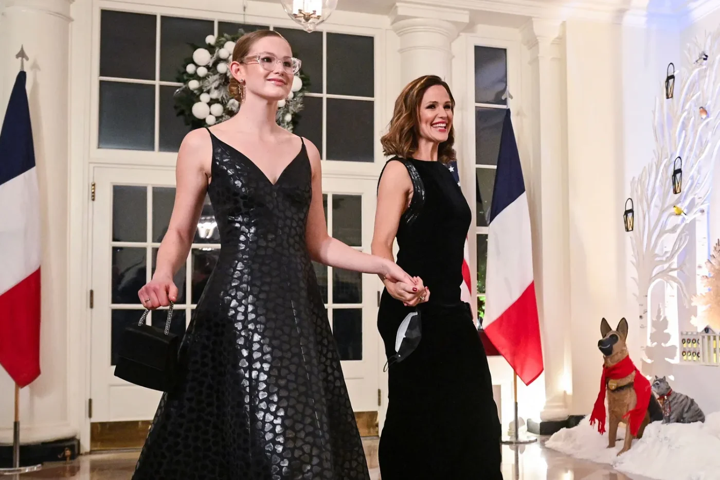 Jennifer Garner and another person walking in formal attire flags and decorations visible in the background