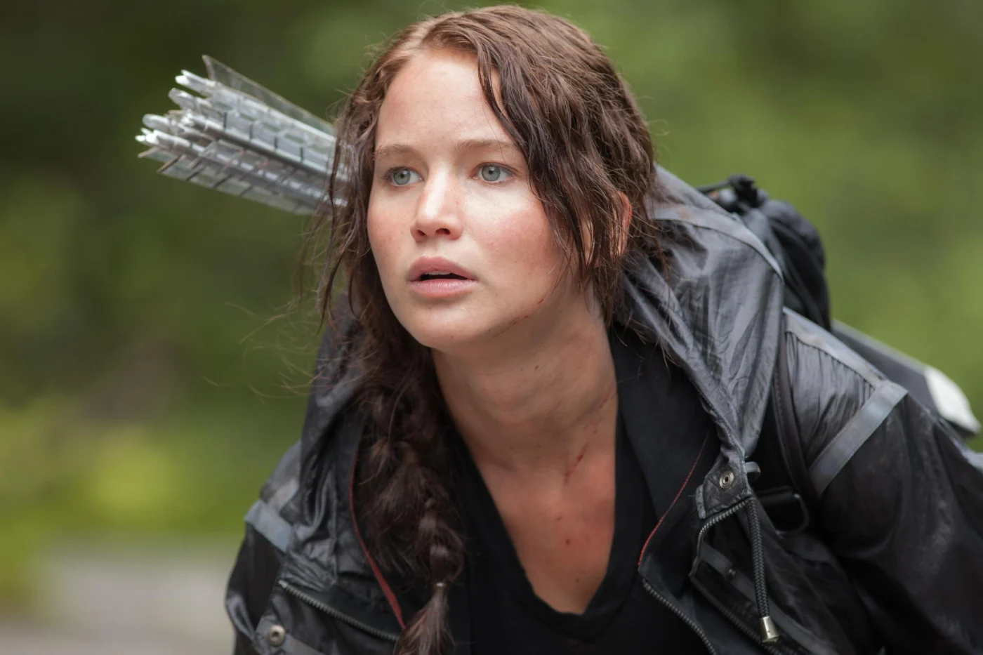 Jennifer Lawrence as Katniss Everdeen on the set of The Hunger Games, wearing a jacket and carrying arrows.