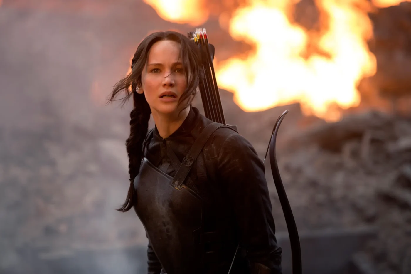 Jennifer Lawrence as Katniss Everdeen with a bow and arrows in front of a fire in The Hunger Games: Mockingjay - Part 1.