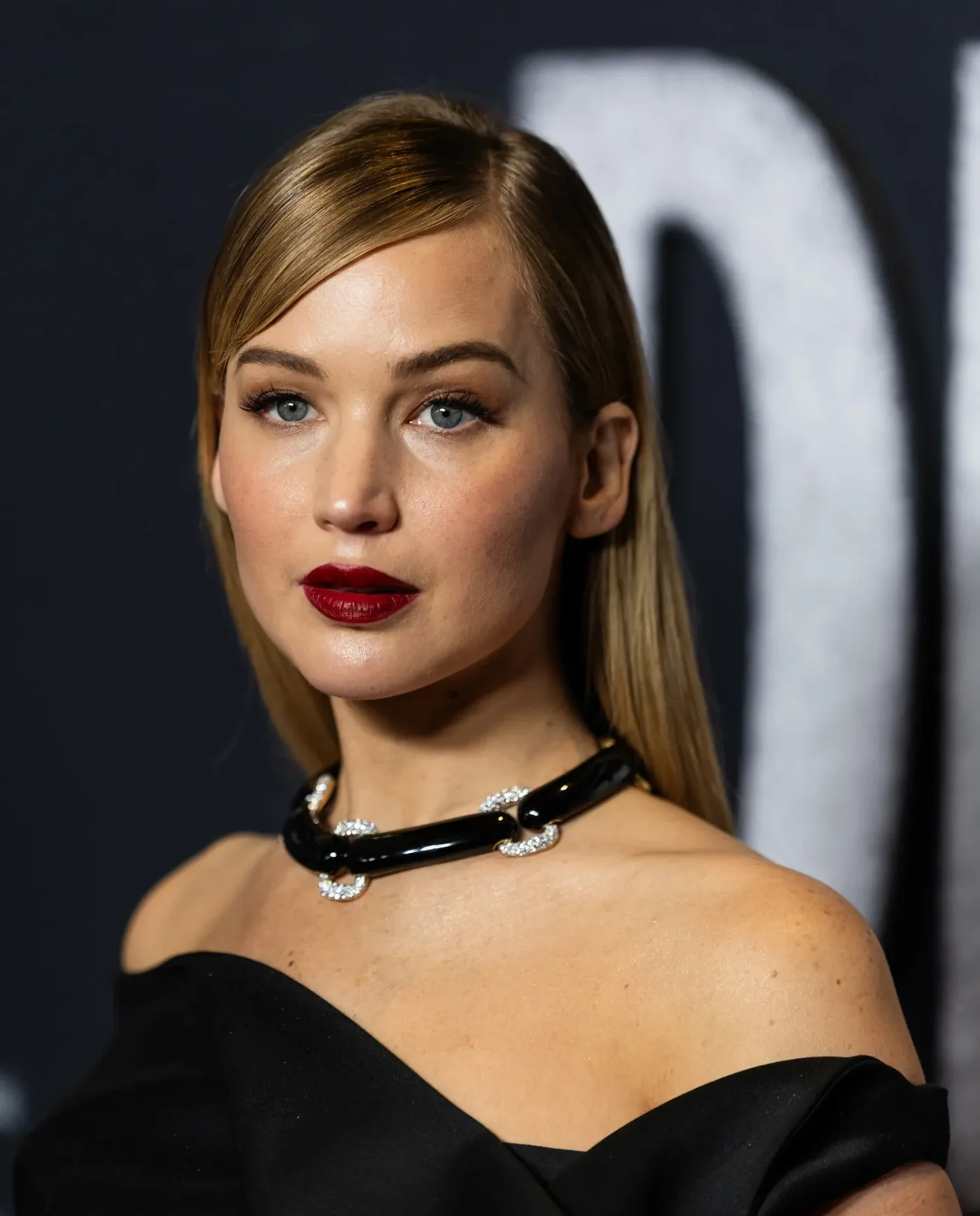 Jennifer Lawrence at a formal event wearing a black outfit with a necklace looking to the side