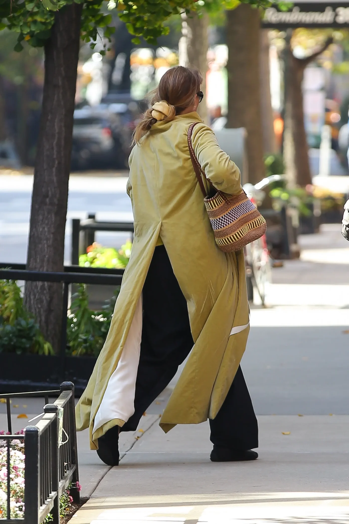Jennifer Lawrence walks down a New York City sidewalk in a long coat and carrying a patterned bag.