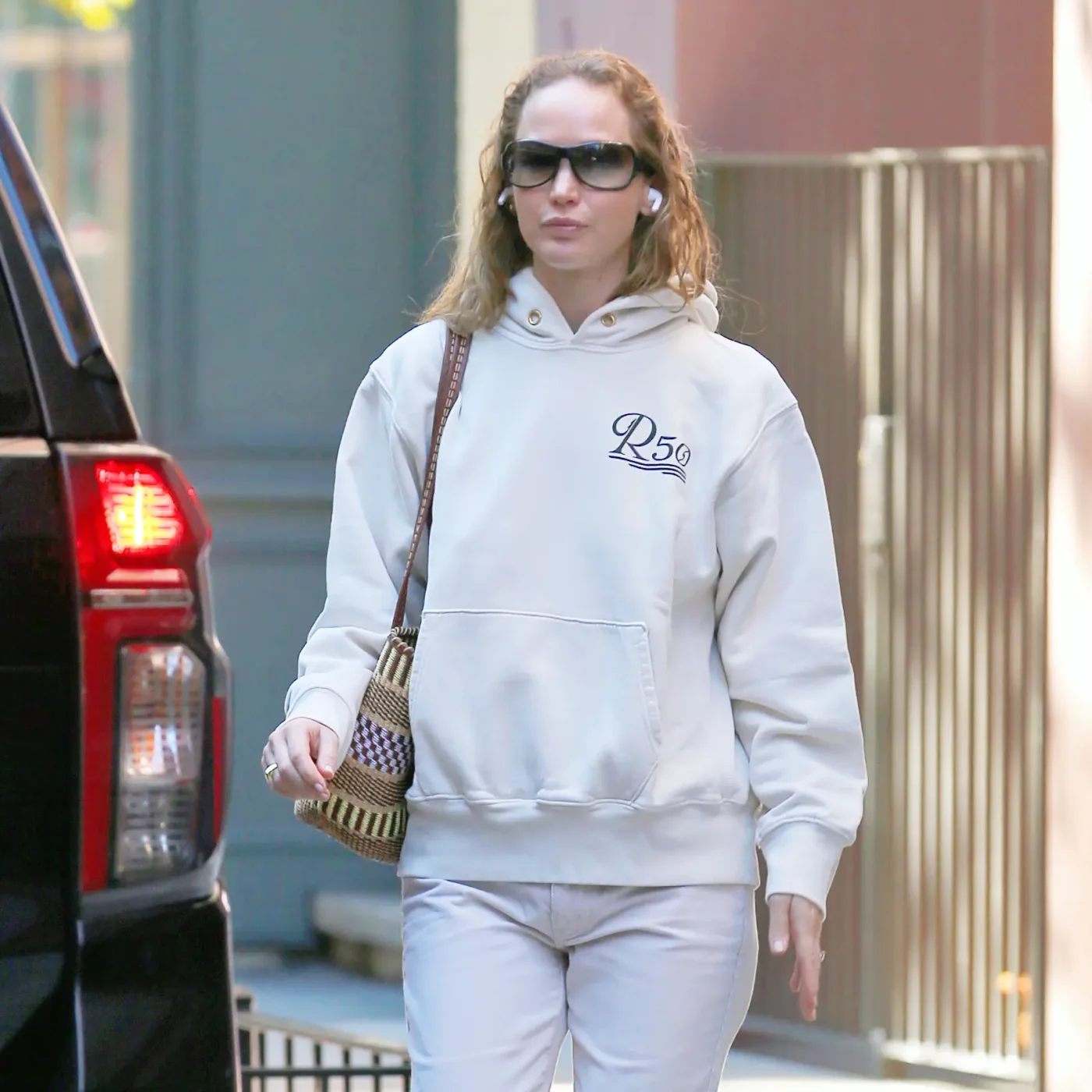 Jennifer Lawrence wearing a white hoodie, khakis, and gradient sunglasses in New York City.