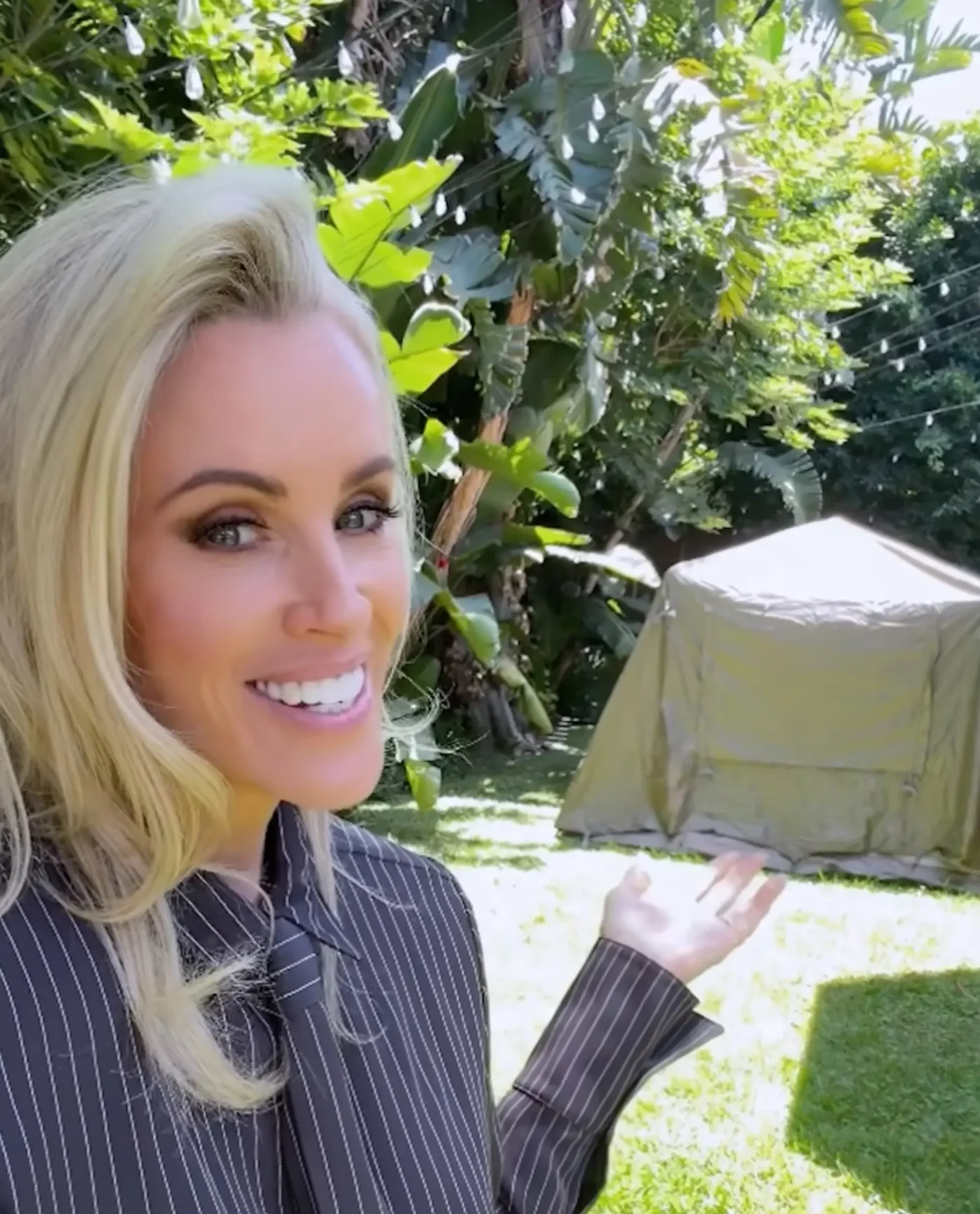 Jenny McCarthy gestures toward a tent set up outdoors in a yard.