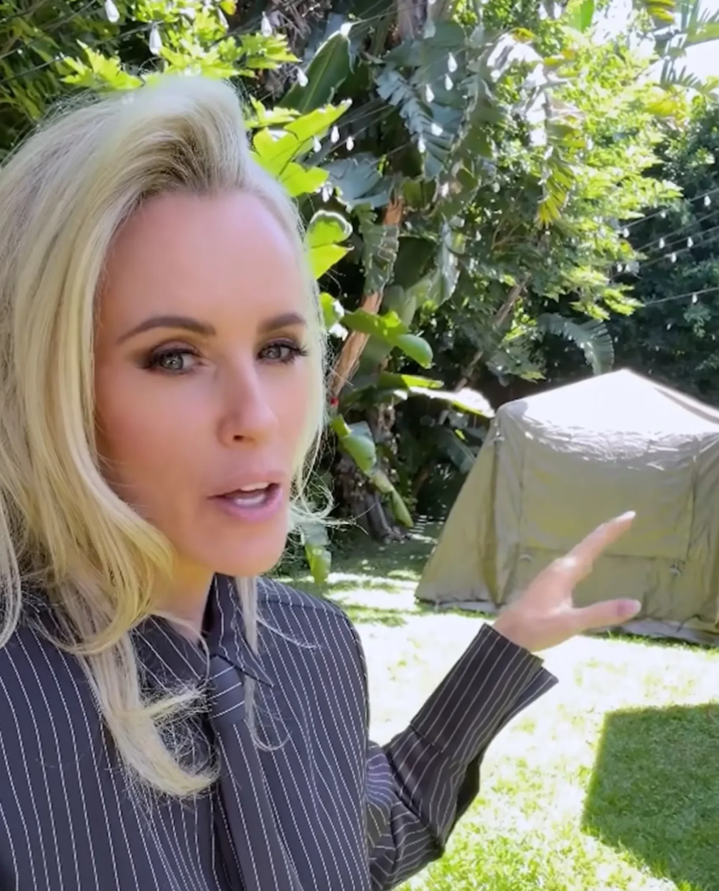 Jenny McCarthy pointing toward a tent set up in a backyard.