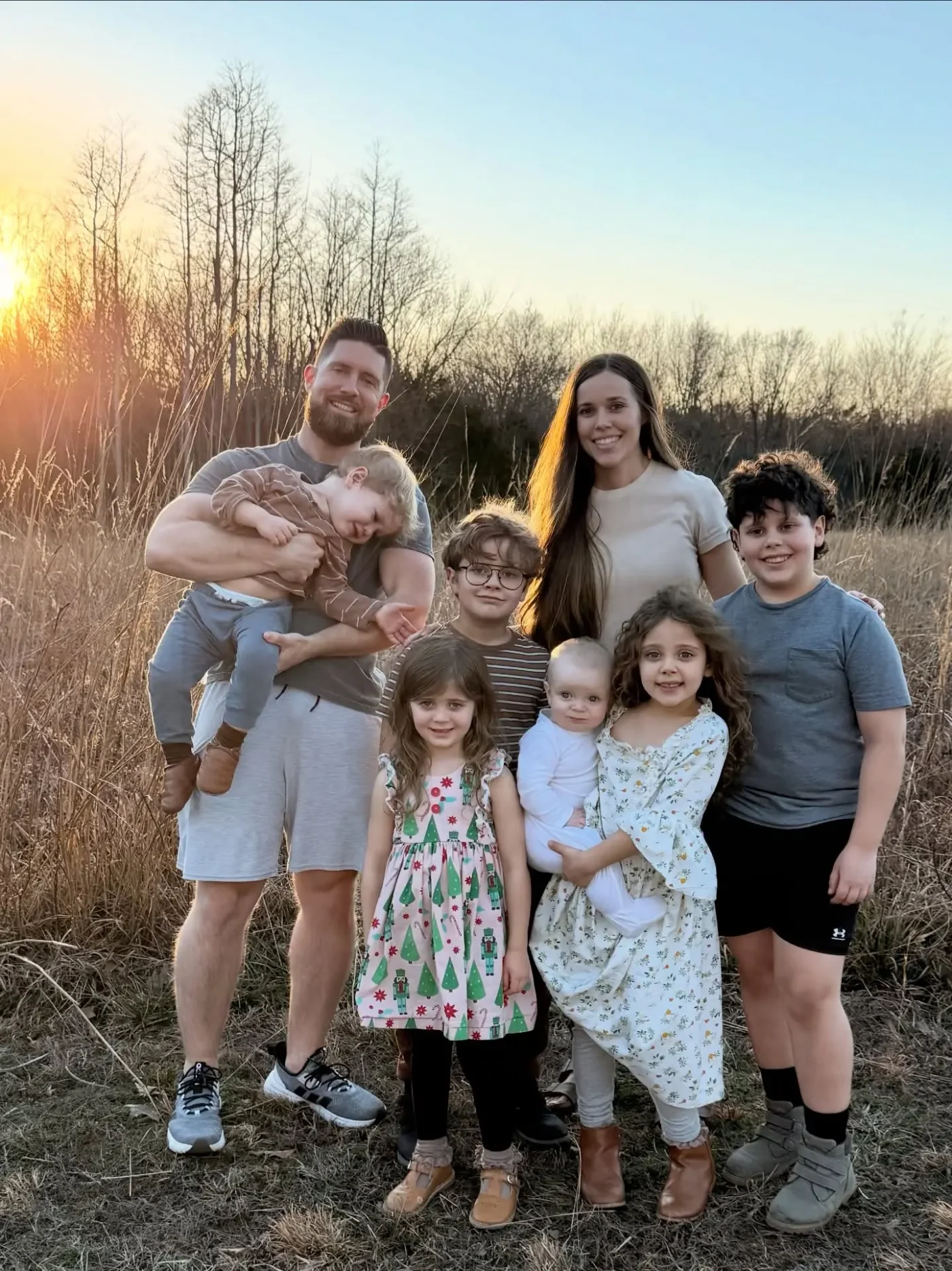 Jessa Duggar and Ben Seewald pose outdoors in a field with their six children during sunset.
