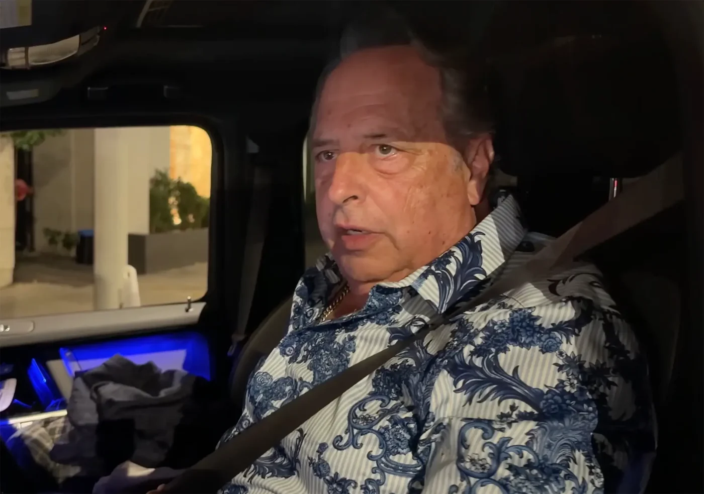 Jon Lovitz sitting in the passenger seat of a car.