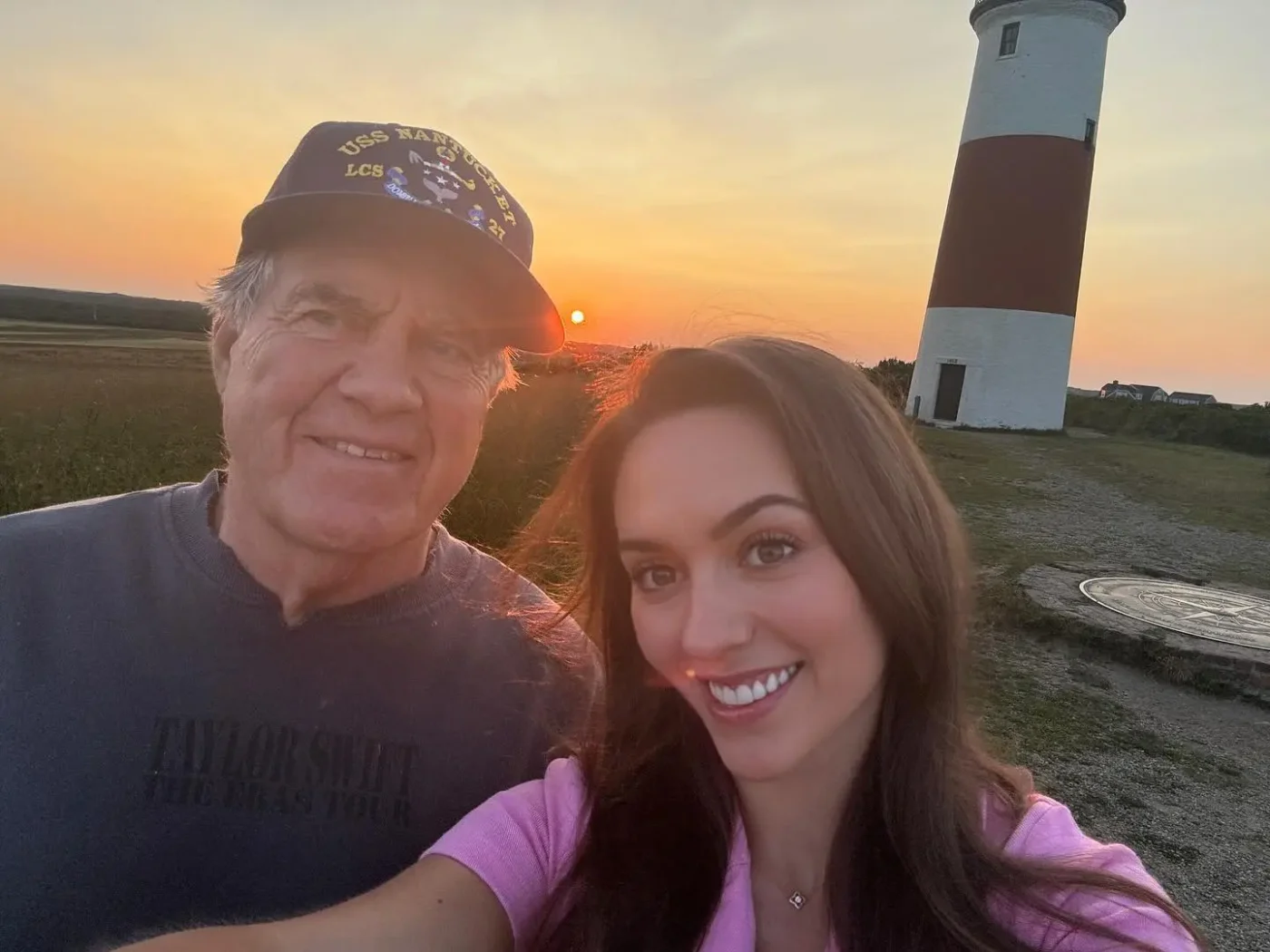 Jordon Hudson taking a selfie with Bill Belichick in front of a lighthouse at sunset.